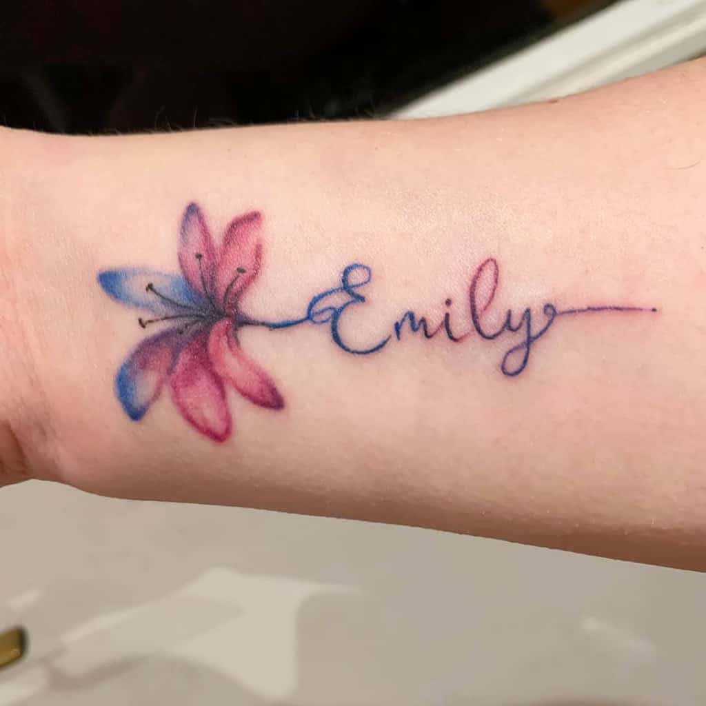 Delicate watercolor tattoo of a pink and blue lily seamlessly blending into the name 'Emily' in elegant cursive