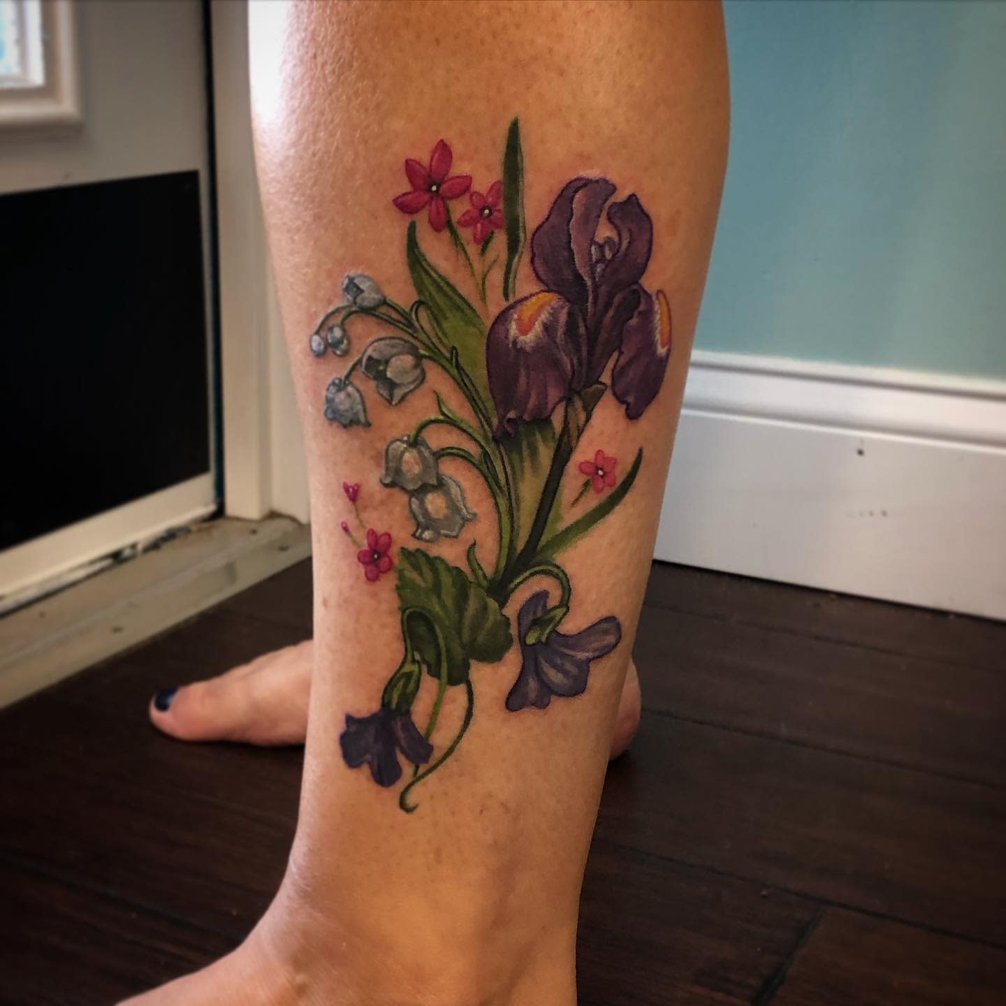 Colorful flower tattoo featuring lilies, irises, and other flowers on a lower leg