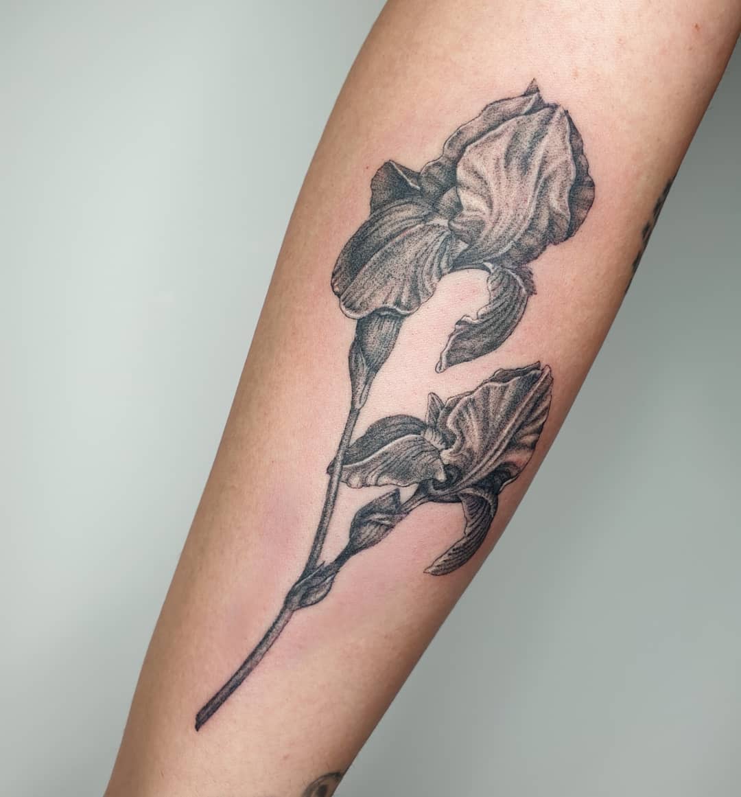 Black and white tattoo of two iris flowers on a forearm