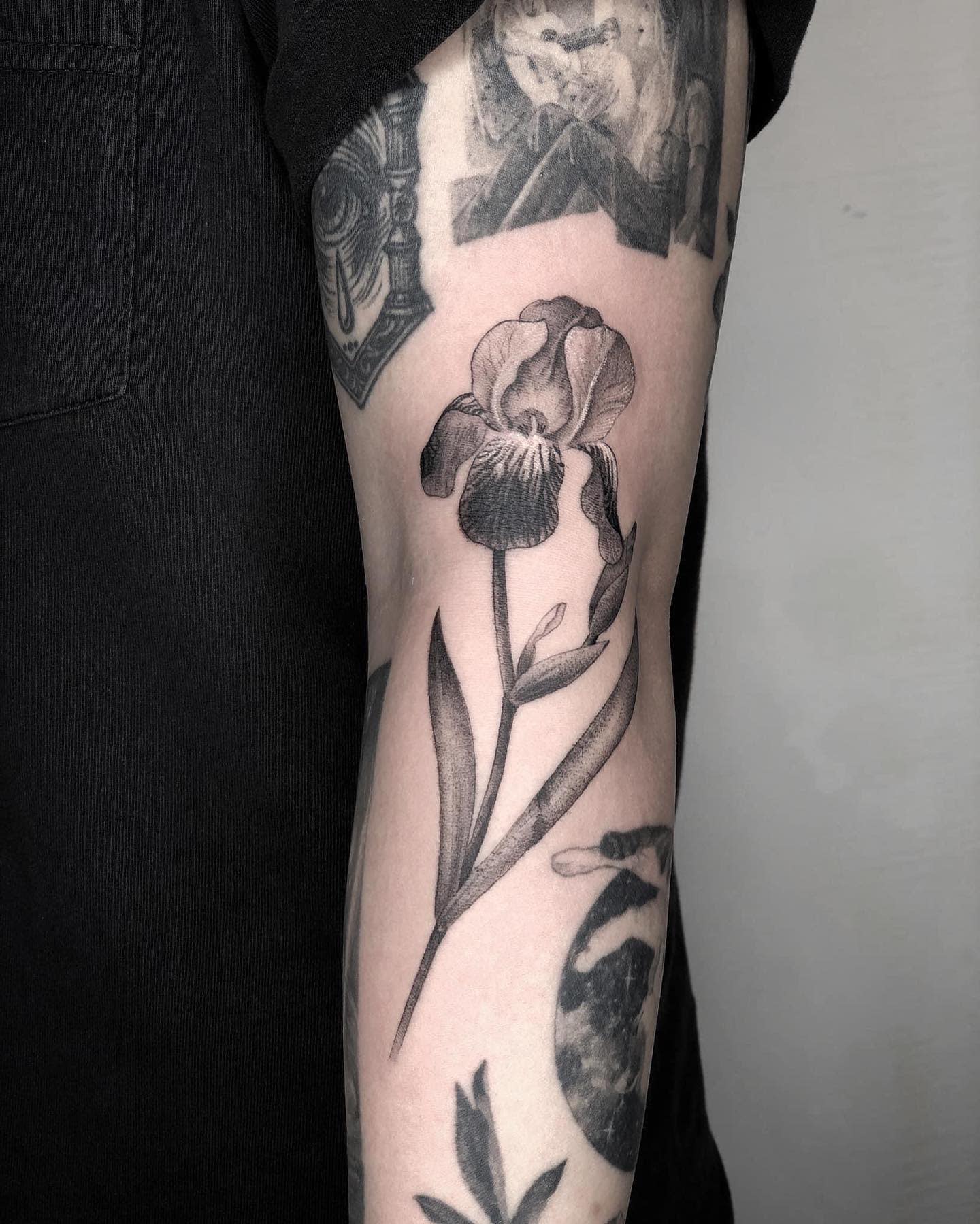 Black and white iris flower tattoo on the back of an upper arm, surrounded by other tattoos