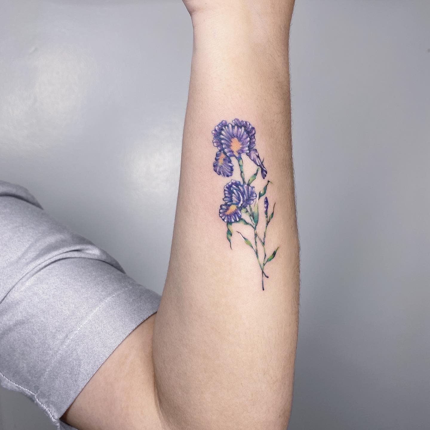 Forearm tattoo of purple flowers with green stems and leaves