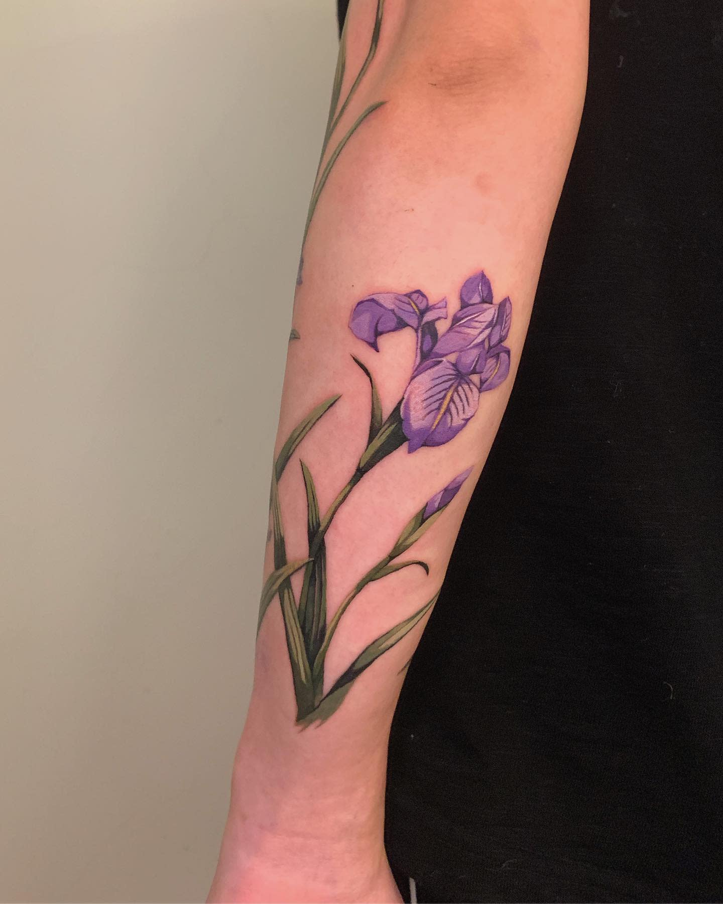 Forearm tattoo of a purple iris flower with green leaves