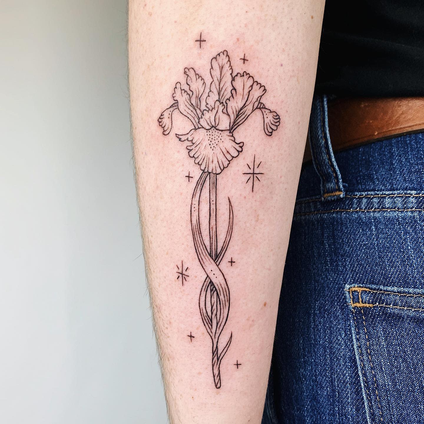 Linework floral tattoo of an iris with sparkles on the forearm