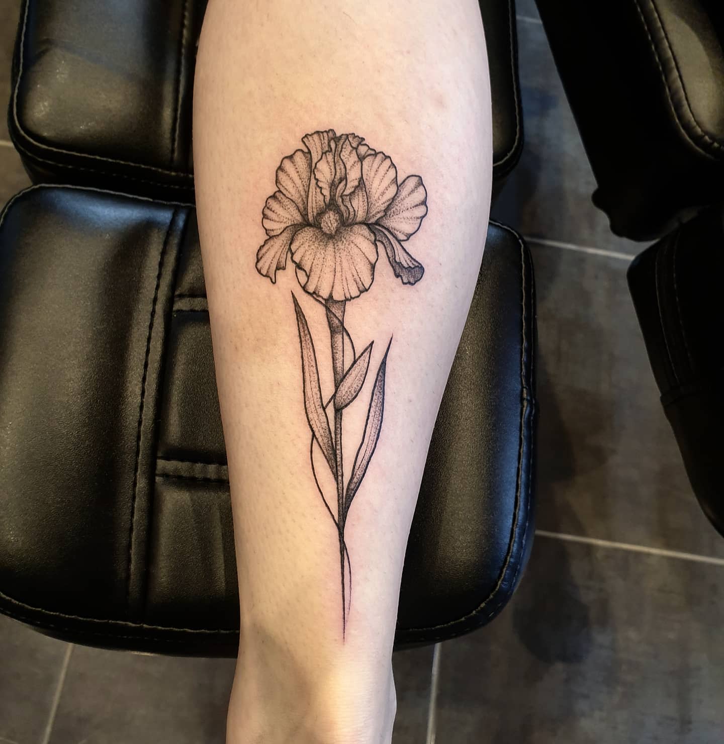A detailed black and grey iris flower tattoo on a calf