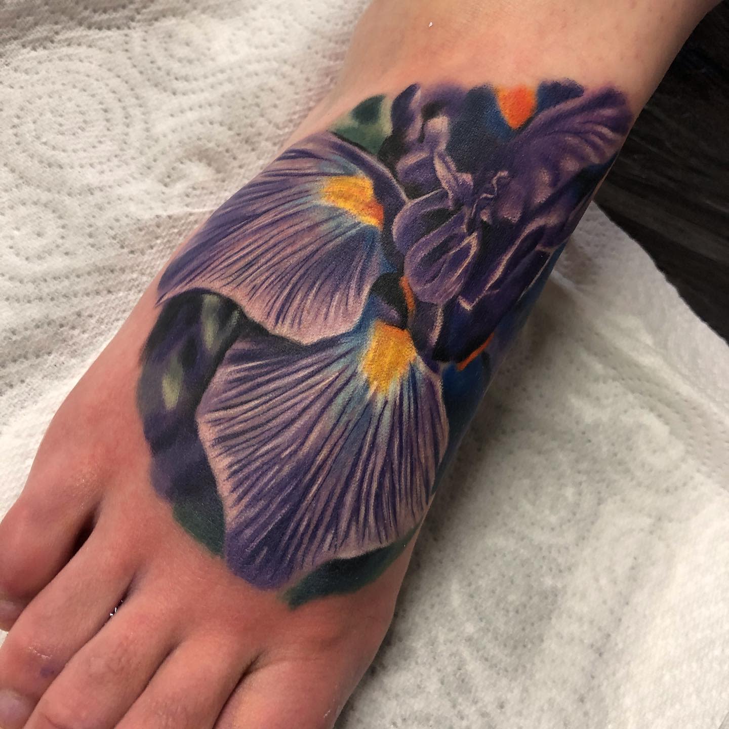 A detailed, purple and yellow iris tattoo on top of a foot