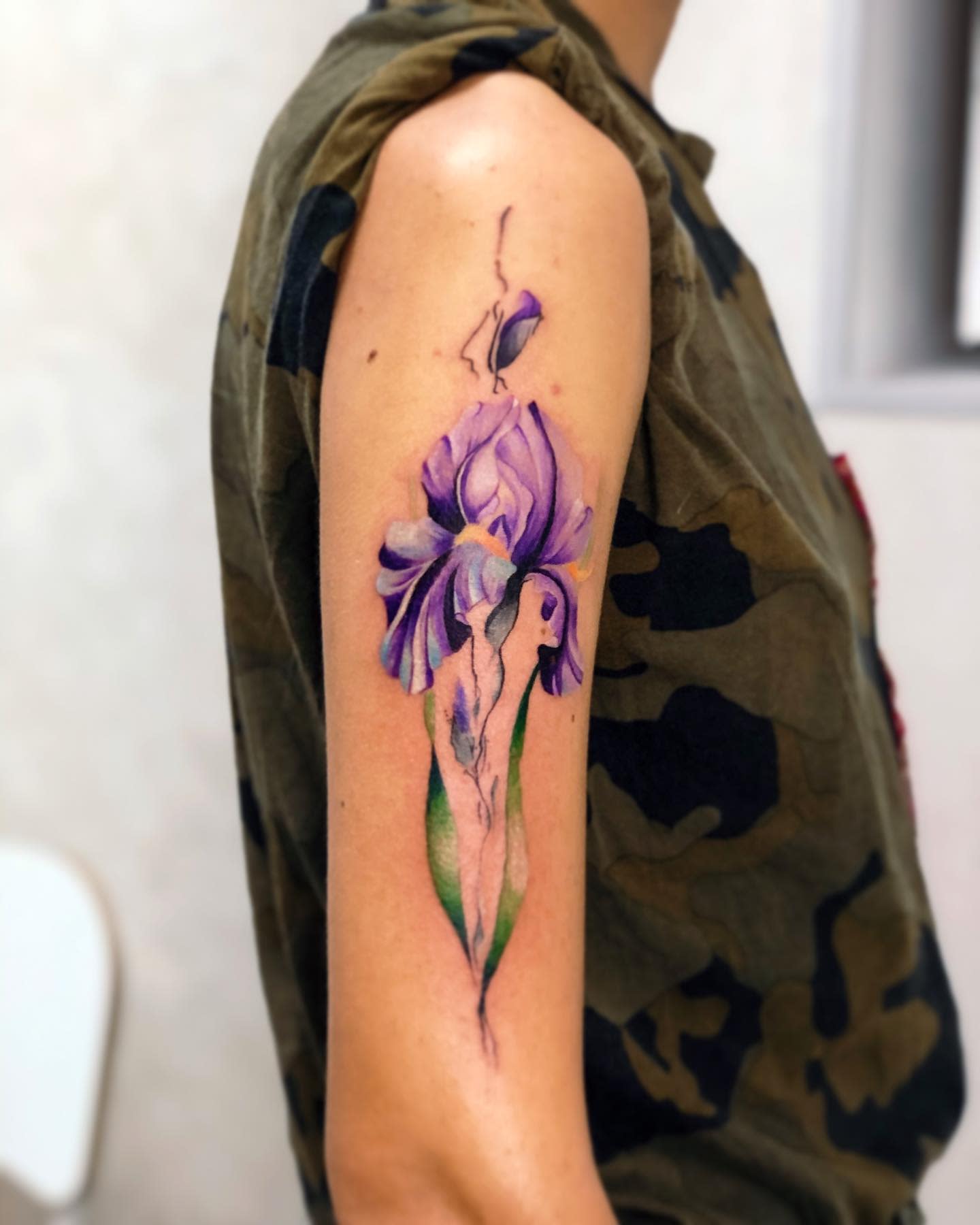 Tattoo of a purple iris flower with green leaves on an upper arm