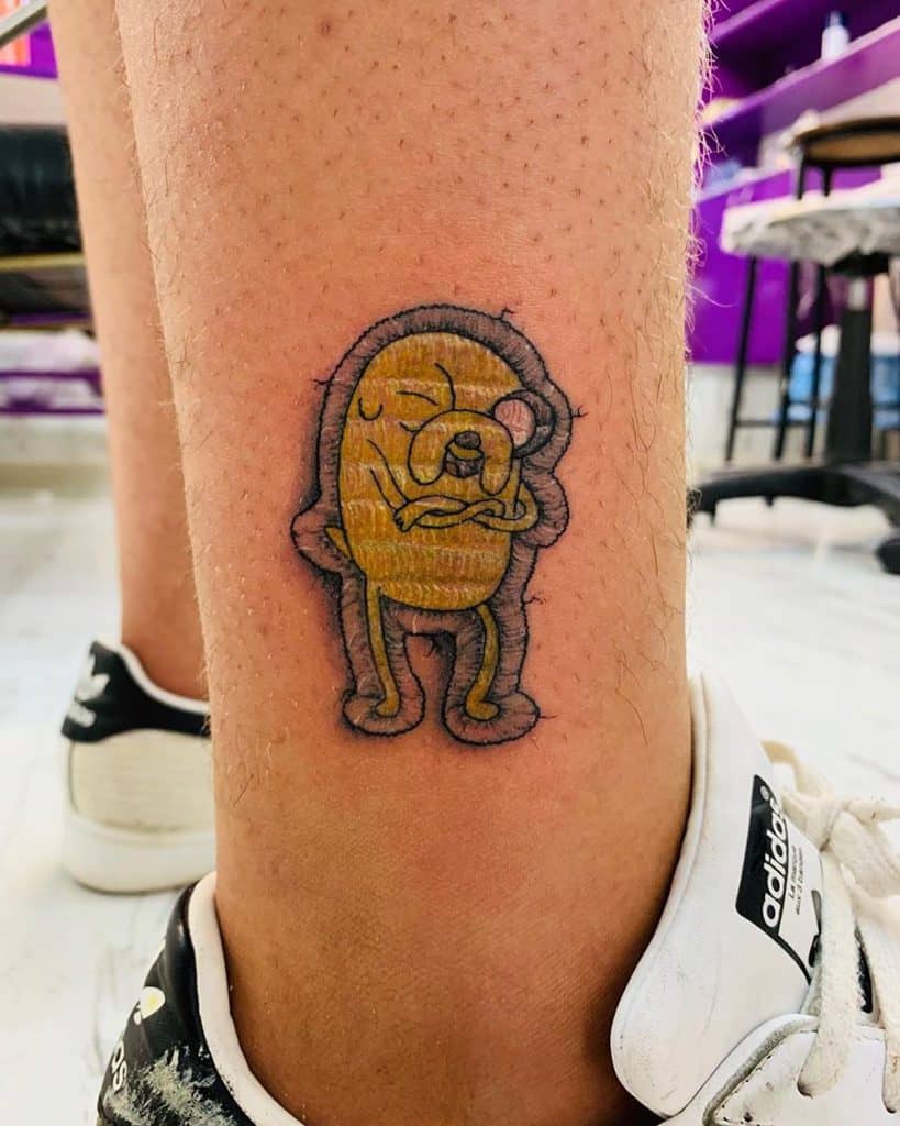 Stitch-inspired tattoo of Jake the Dog in a chill pose, mimicking a sewn-on patch with quilted fabric details.