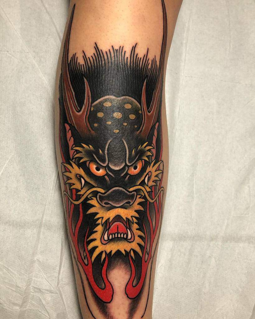 A tattoo of a dragon head with fierce features and bold colors adorns someone's leg