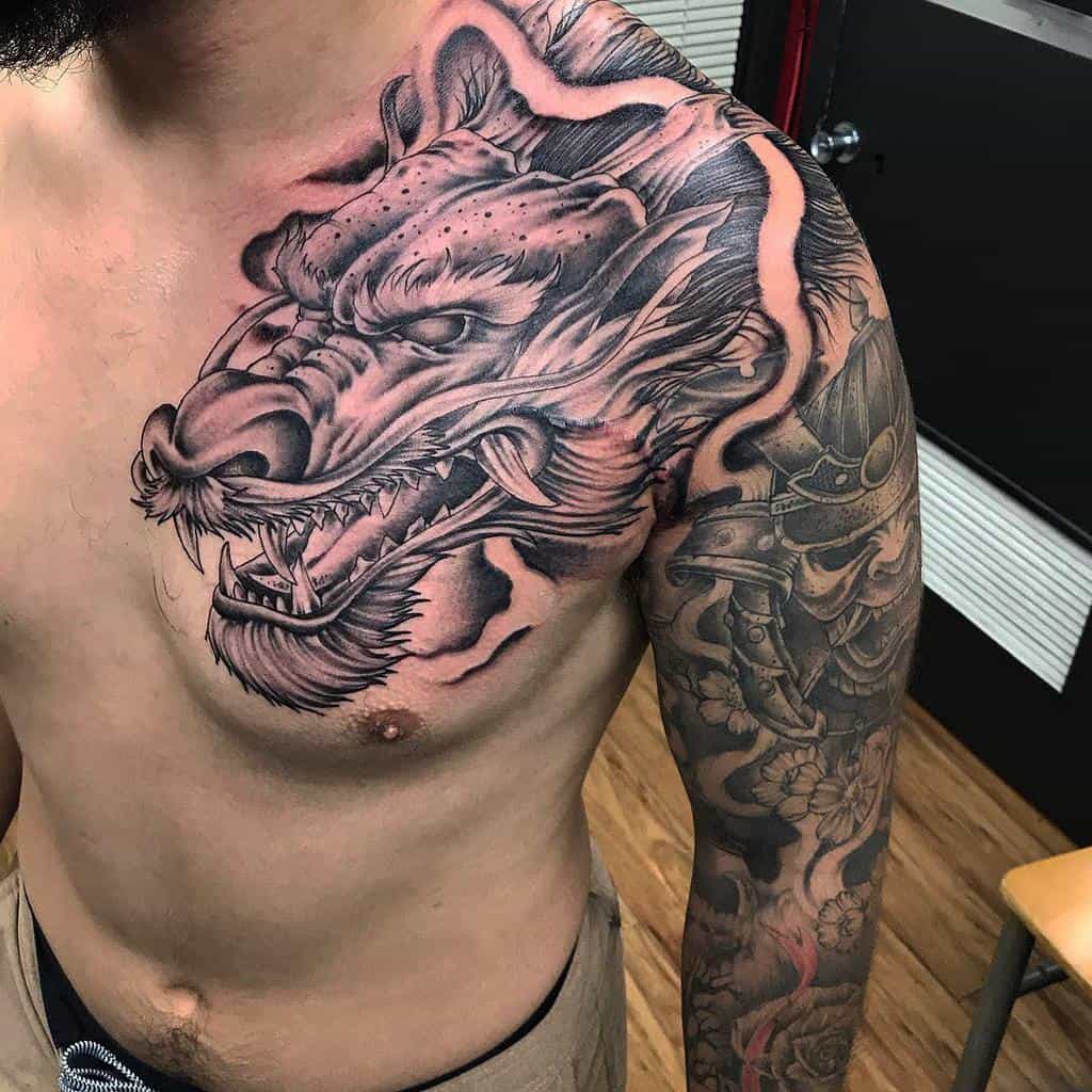 Man with a detailed dragon tattoo covering his chest and arm, intricately designed in black and grey ink, with the dragon's head expertly crafted adding an intense focal point to the artwork