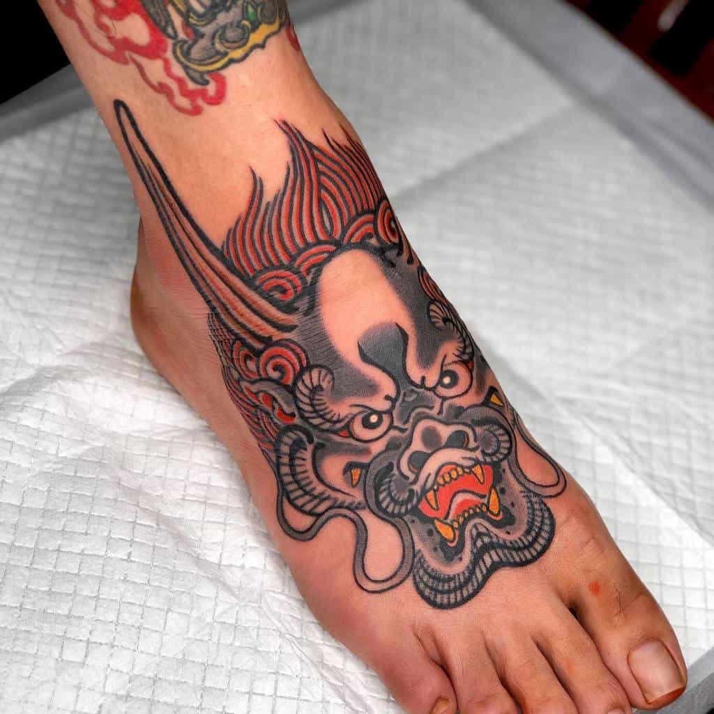 A Japanese style tattoo of a fierce dragon head adorns the person's foot, showcasing vivid red and black ink details
