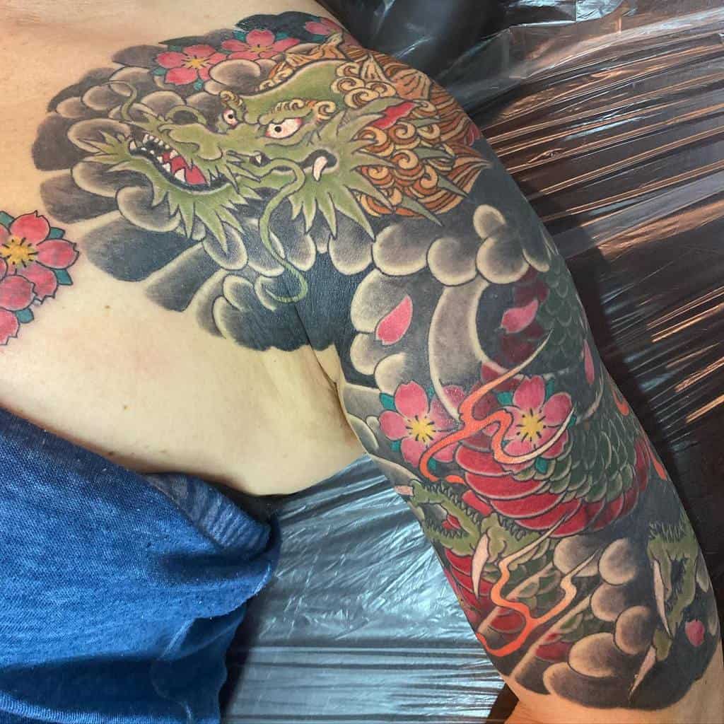 Colorful dragon tattoo sleeve with red flowers and swirling clouds on an upper arm
