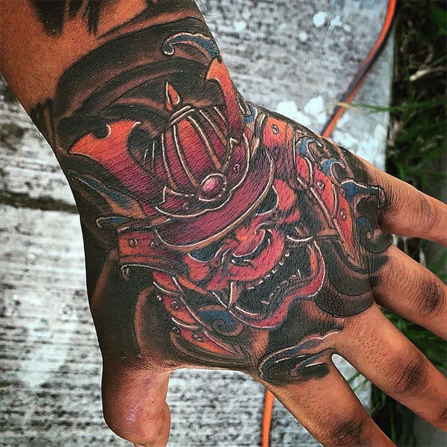Bold hand tattoo featuring a fierce red samurai mask with intricate details and vibrant orange and blue accents for a striking design