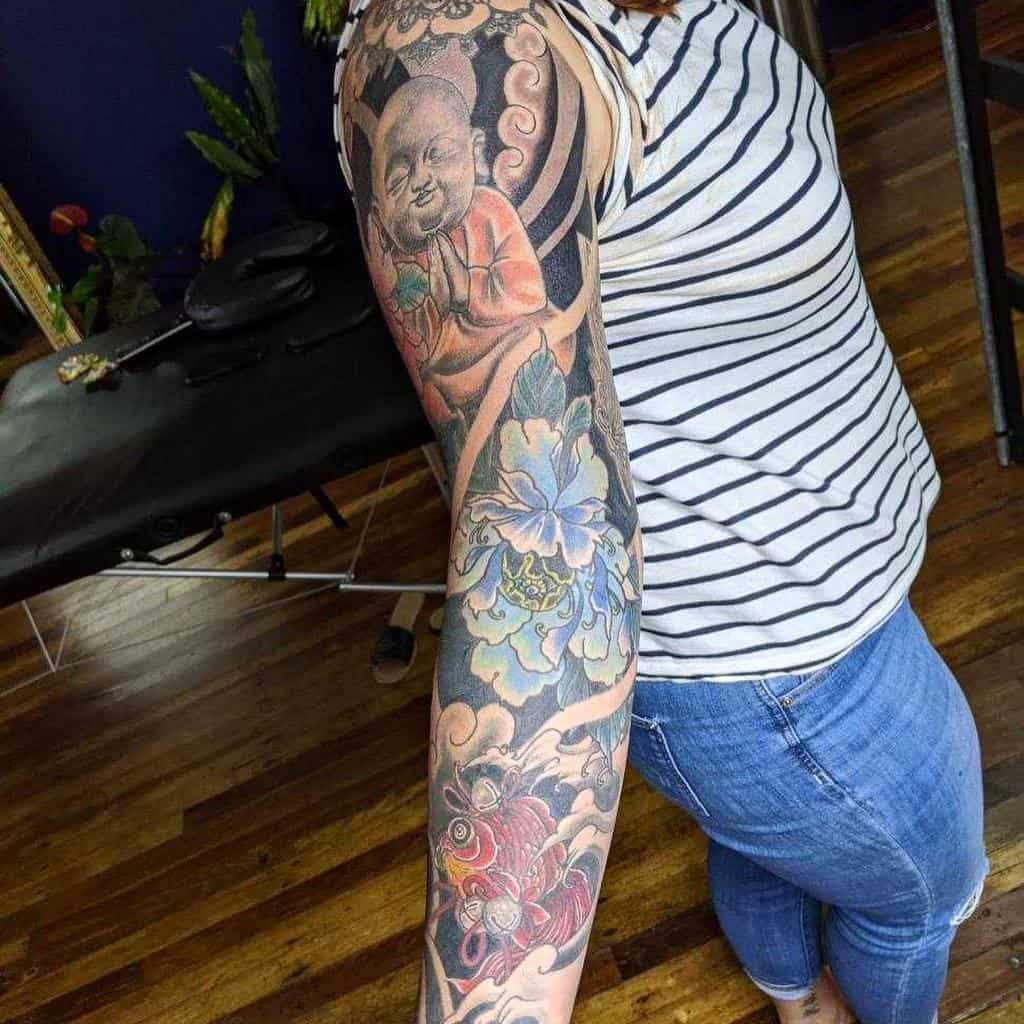 Intricate Japanese sleeve tattoo showcasing a serene Buddha figure, colorful koi fish, and vibrant floral designs