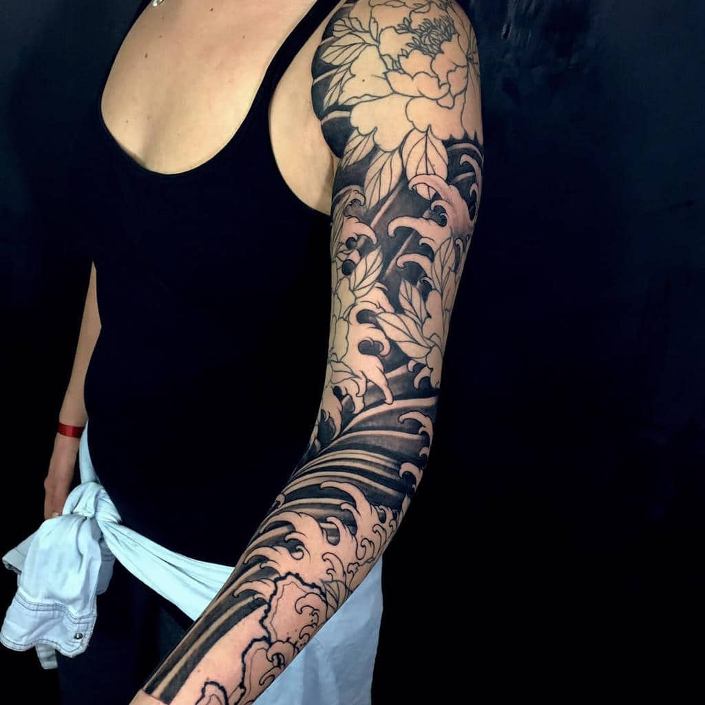 This Japanese-inspired sleeve tattoo highlights bold wave patterns combined with delicate floral elements, creating a striking balance of movement and elegance