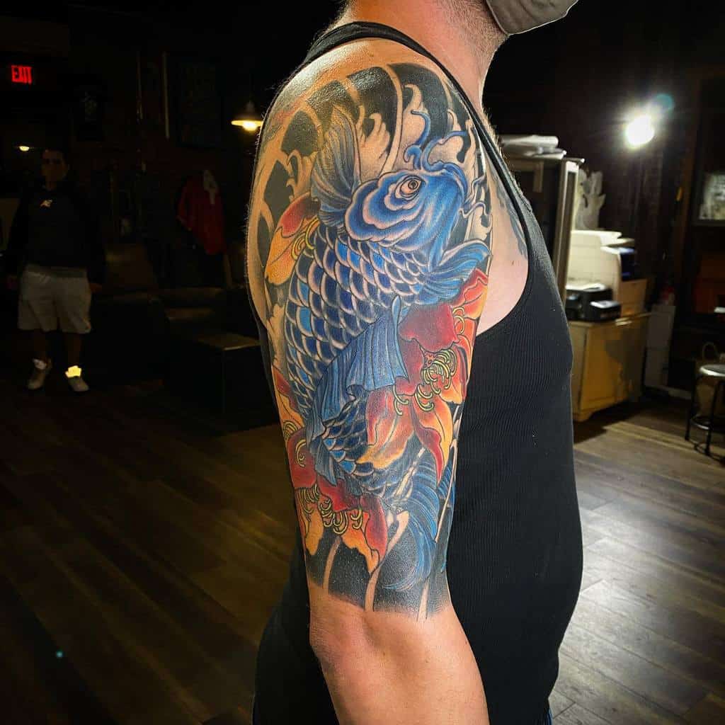 A man's arm with a detailed blue koi fish tattoo surrounded by colorful waves and floral designs