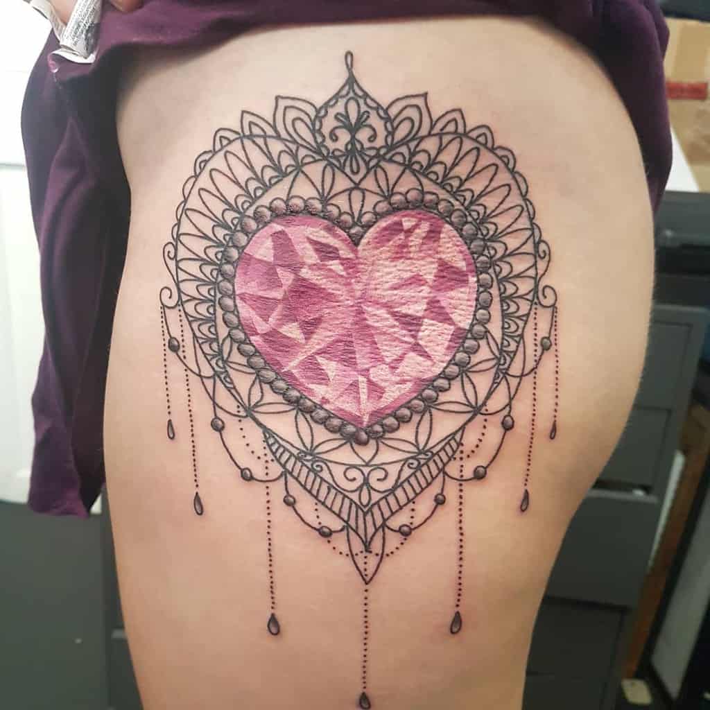 Elegant tattoo featuring a faceted pink gemstone heart framed by intricate mandala patterns, pearl-like beads, and chandelier-style teardrop accents
