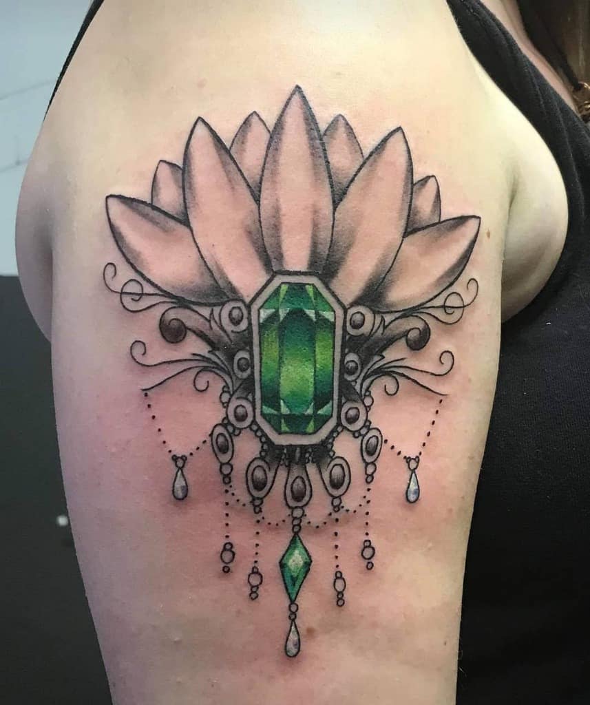 Elegant tattoo featuring a large shaded lotus flower with a faceted green gemstone at the center, surrounded by intricate filigree and chandelier-style teardrop beads