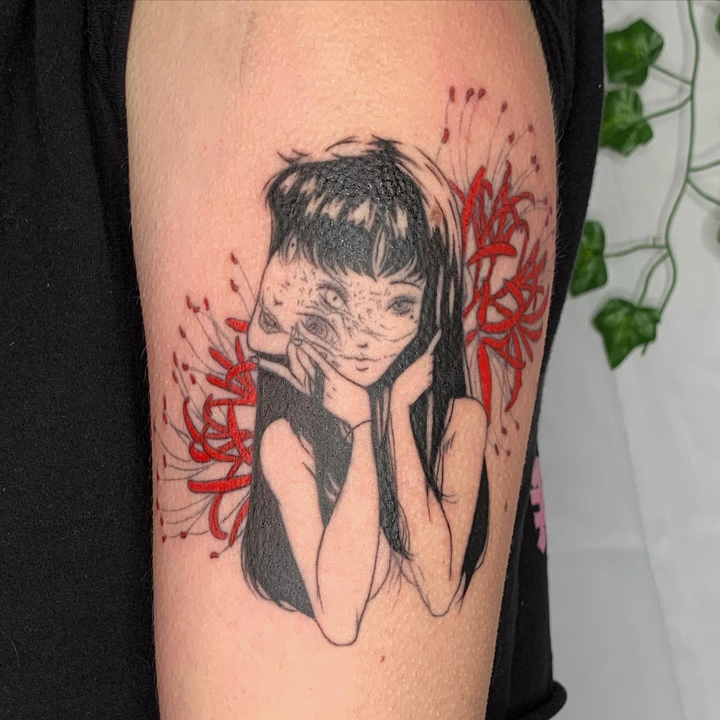 Arm tattoo of a Junji Ito character with her face partly melting, surrounded by red flowers