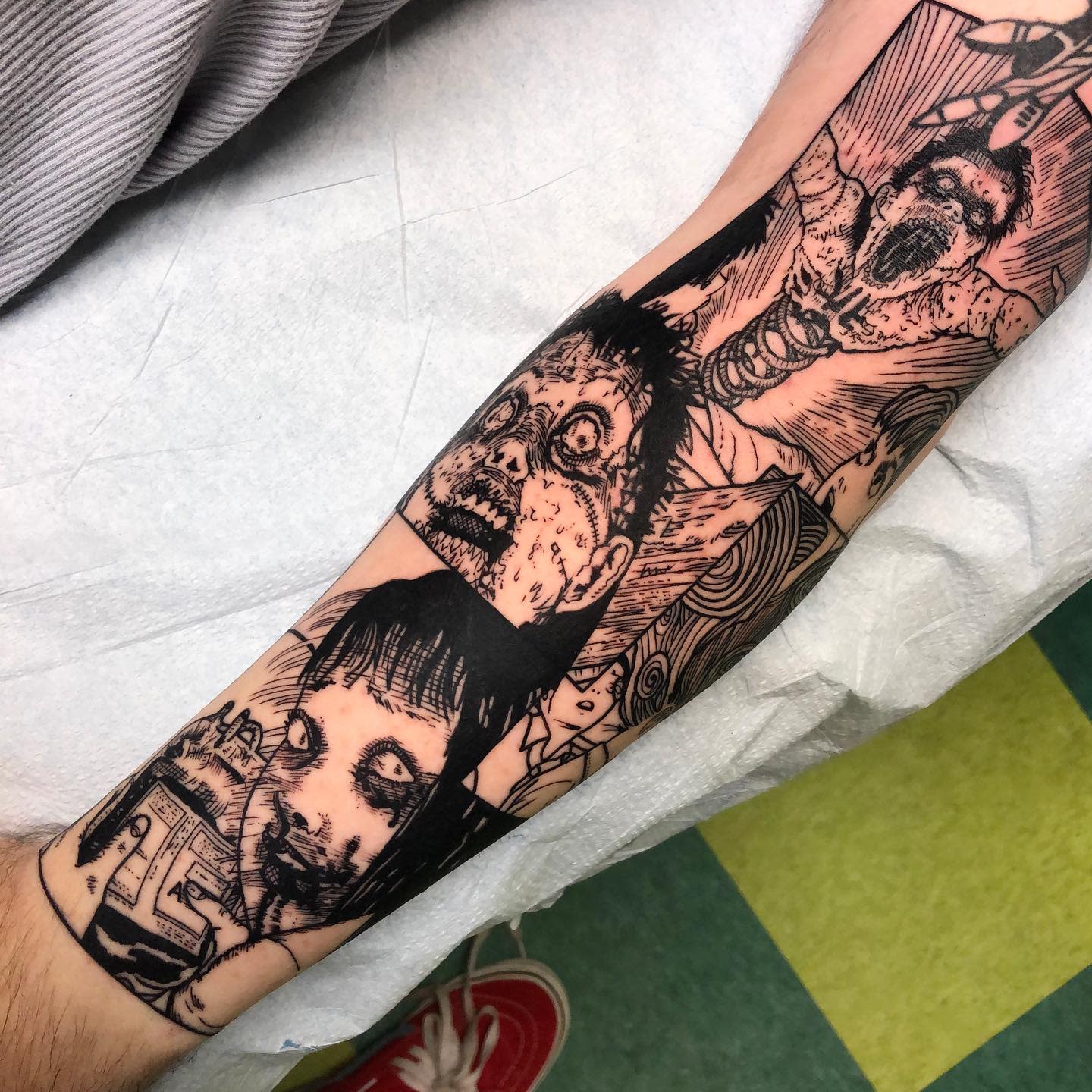 Forearm tattoo featuring multiple horror panels from Junji Ito, depicting twisted and grotesque faces