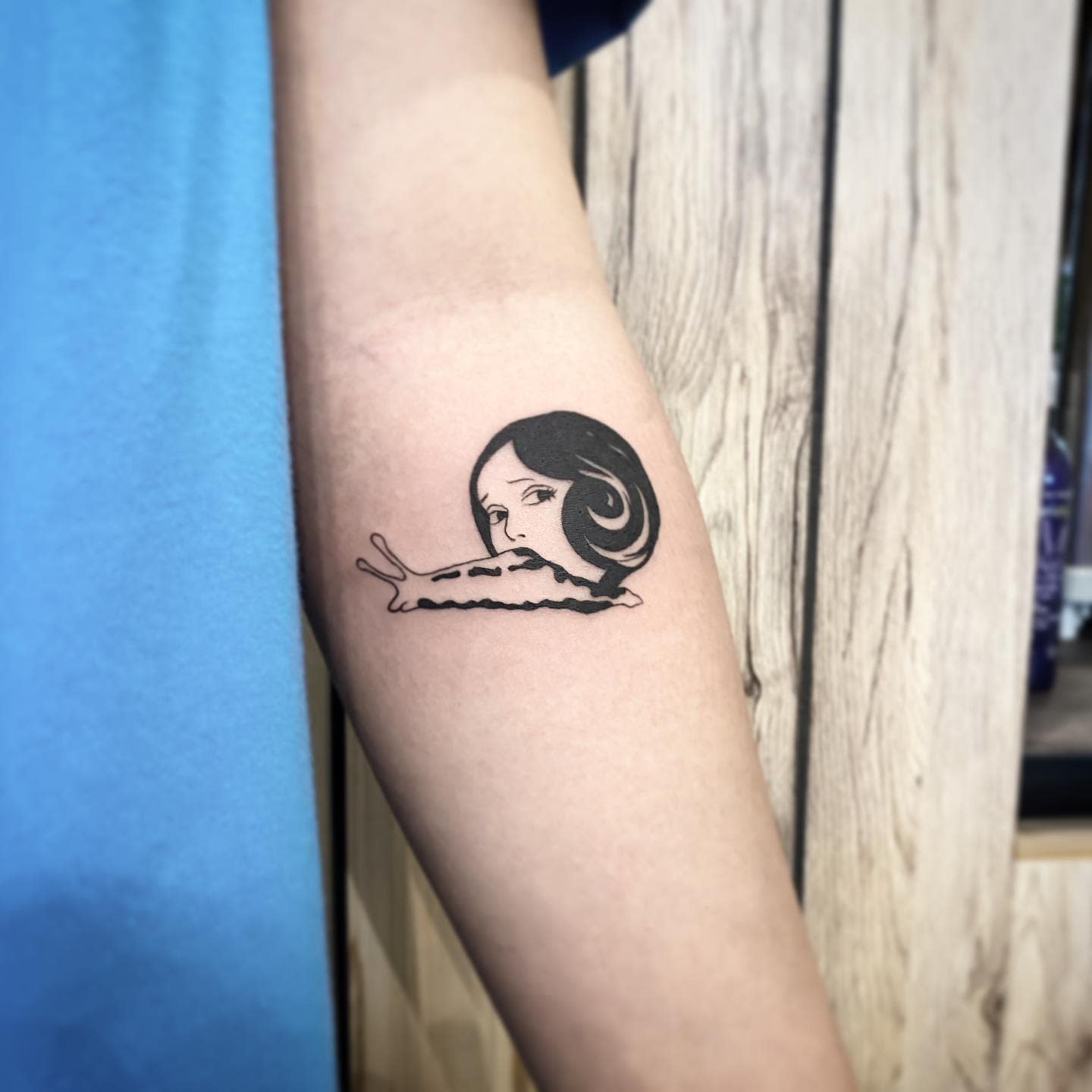 Forearm tattoo of a Junji Ito character's face merging into a snail, reflecting eerie transformation
