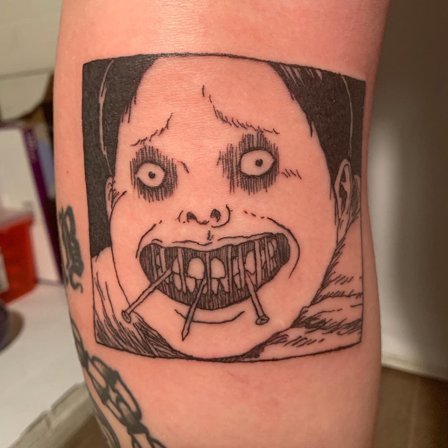 Forearm tattoo of Souichi from Junji Ito, grinning eerily with nails in his mouth, embodying his sinister character