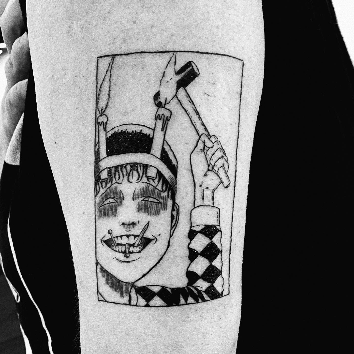 Upper arm tattoo of Souichi from Junji Ito, grinning wickedly while holding a hammer, with nails in his mouth and candles on his head