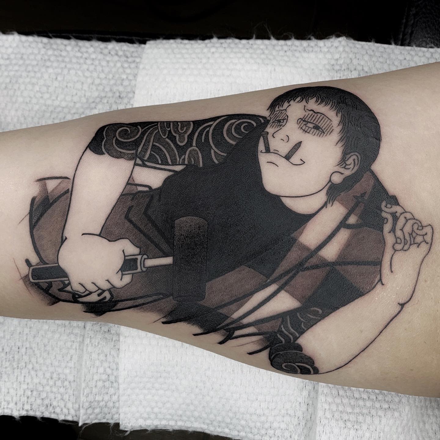 Forearm tattoo of Souichi from Junji Ito, holding a hammer with nails in his mouth, depicted with a sly expression