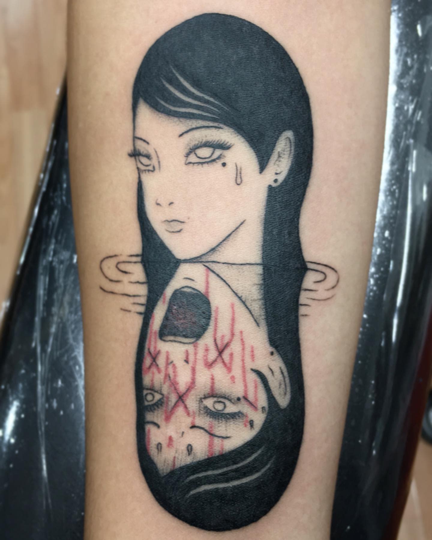 Forearm tattoo of Tomie from Junji Ito, showing her face both calm and mutilated in a mirrored design