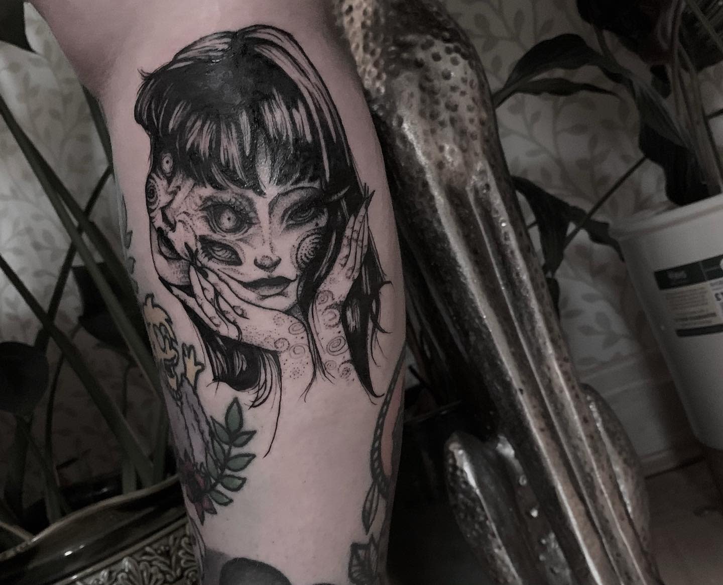 Leg tattoo of Junji Ito's Tomie with her face grotesquely distorted, capturing her eerie transformation