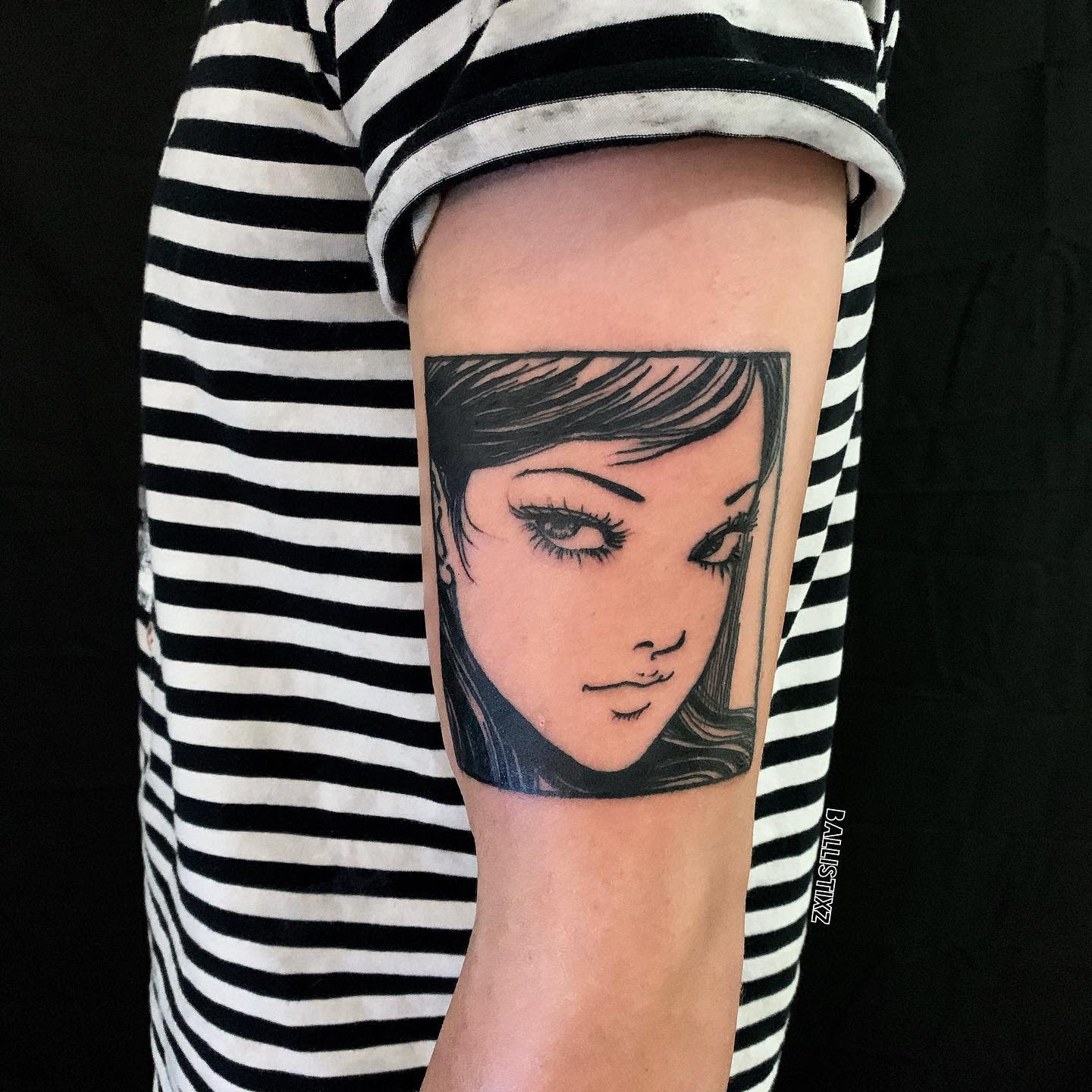 Upper arm tattoo of Tomie from Junji Ito, featuring her iconic, alluring gaze in a clean, bold style