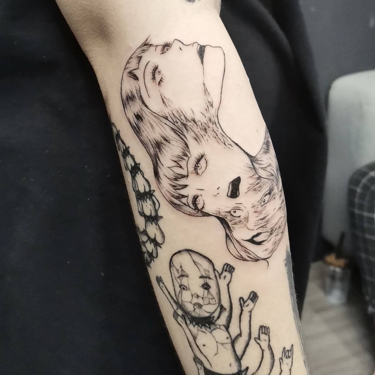 Forearm tattoo of Junji Ito's Tomie, featuring multiple distorted faces blending together, showcasing her unsettling transformation