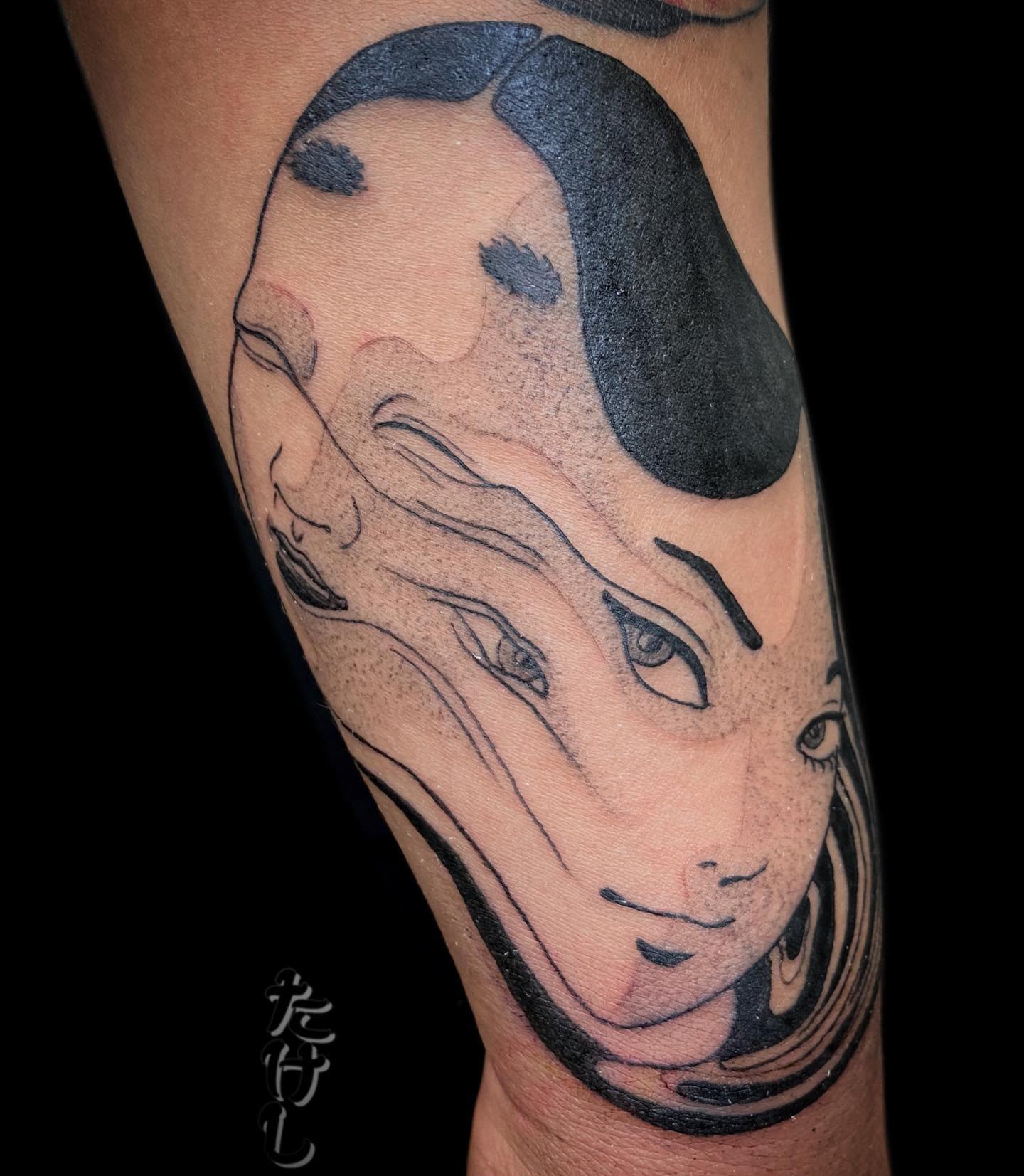 Forearm tattoo of Junji Ito's Tomie, with her face eerily distorted and melting, capturing her unsettling transformation