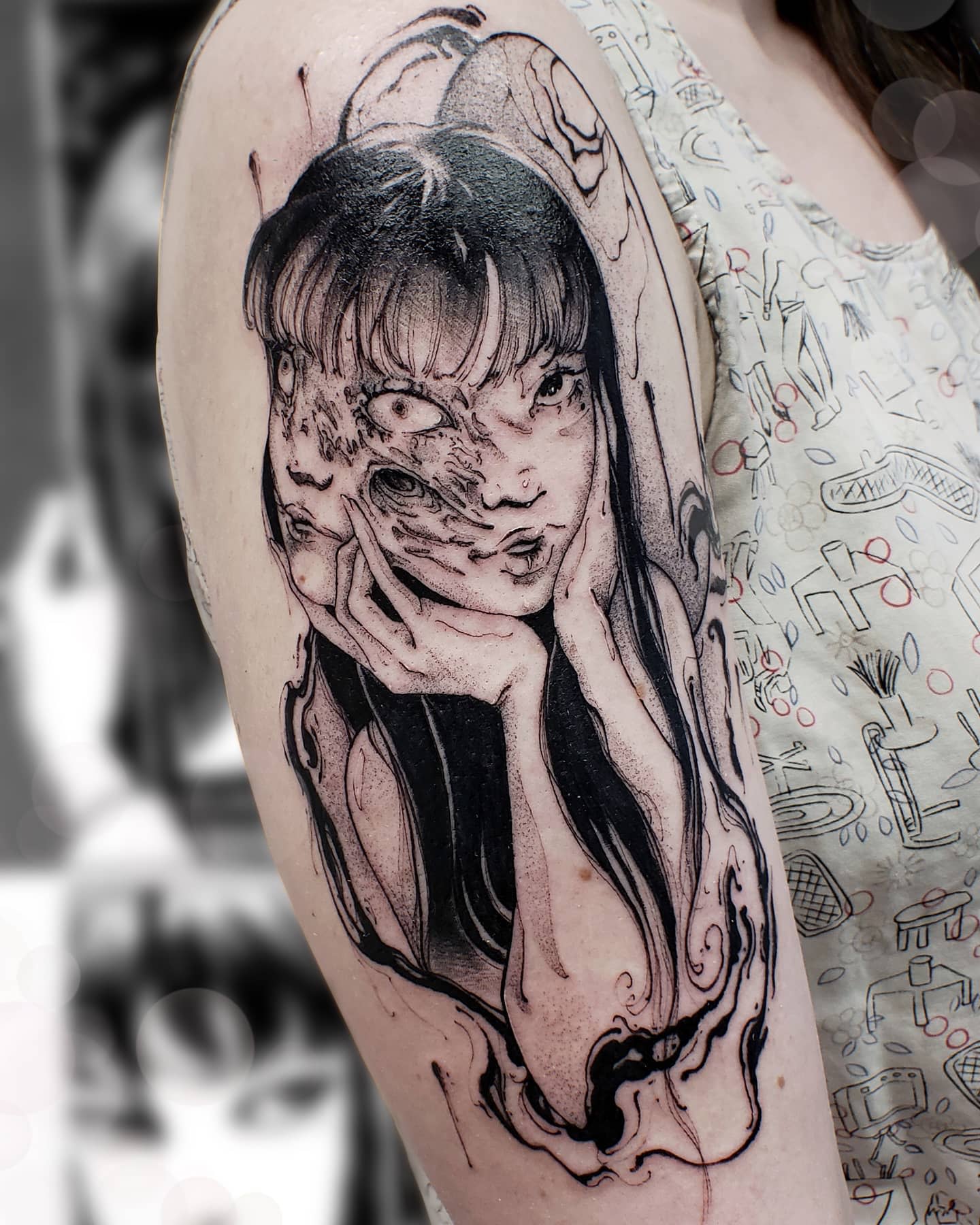 Upper arm tattoo of Junji Ito's Tomie, with her face grotesquely merging and distorting, emphasizing her eerie transformation