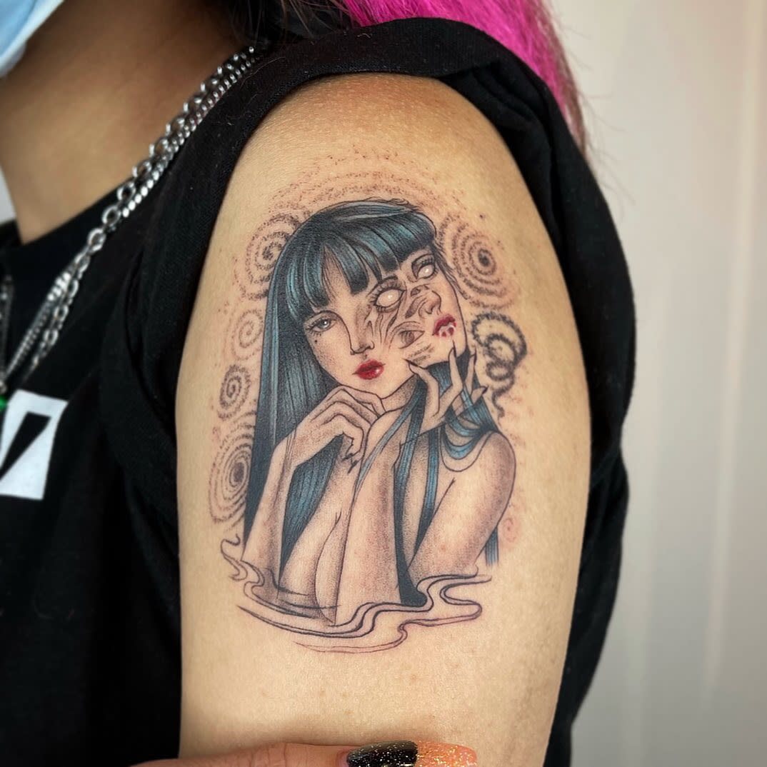 Upper arm tattoo of Junji Ito's Tomie, with a distorted and melting face, surrounded by swirling patterns, blending horror with beauty