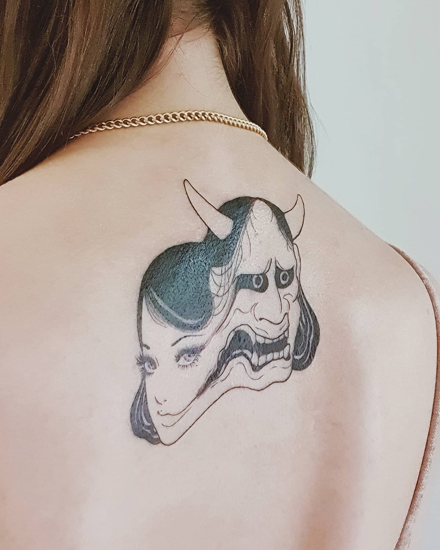 Upper back tattoo of Junji Ito's Tomie, merging with a demonic mask, symbolizing her dual nature of beauty and horror