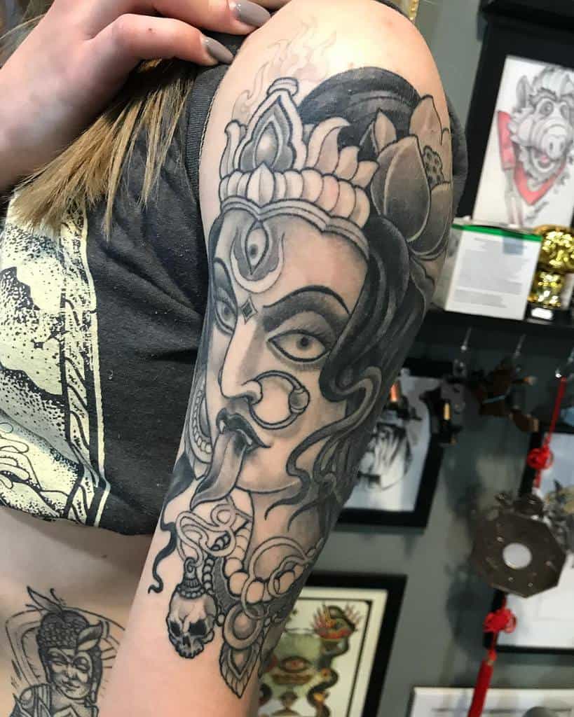 Detailed black and gray Kali tattoo, highlighting her symbolic weapons and skull necklace with flower on her hair