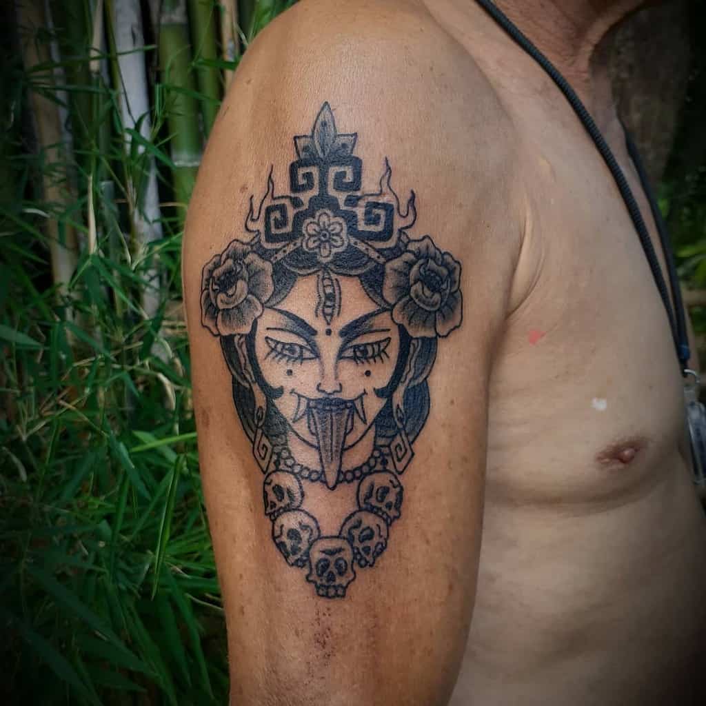 Bold, graphic-style Kali tattoo, featuring thick black lines, a protruding tongue, a skull necklace, and flanking roses