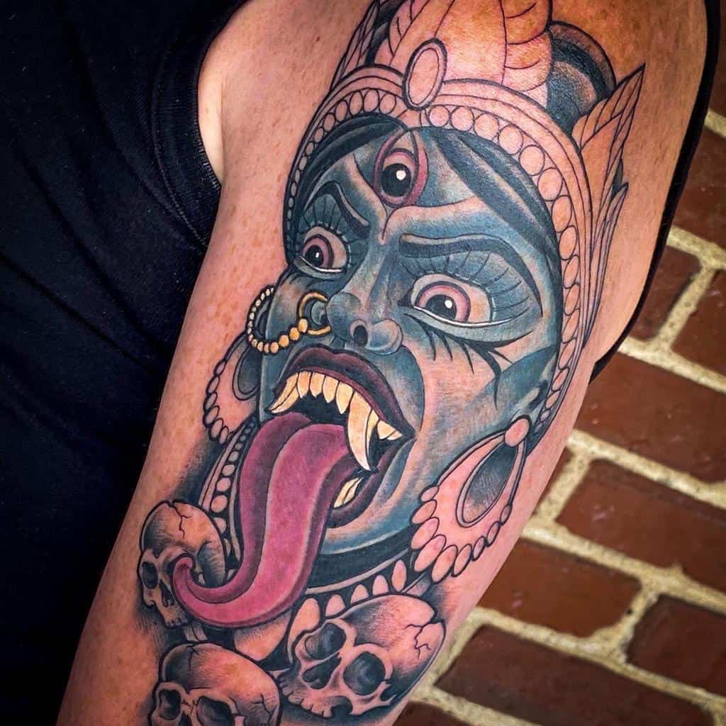 Traditional tattoo style depiction of Kali, showcasing her wide eyes, protruding tongue, decorative crown, jewelry, and a necklace of skulls