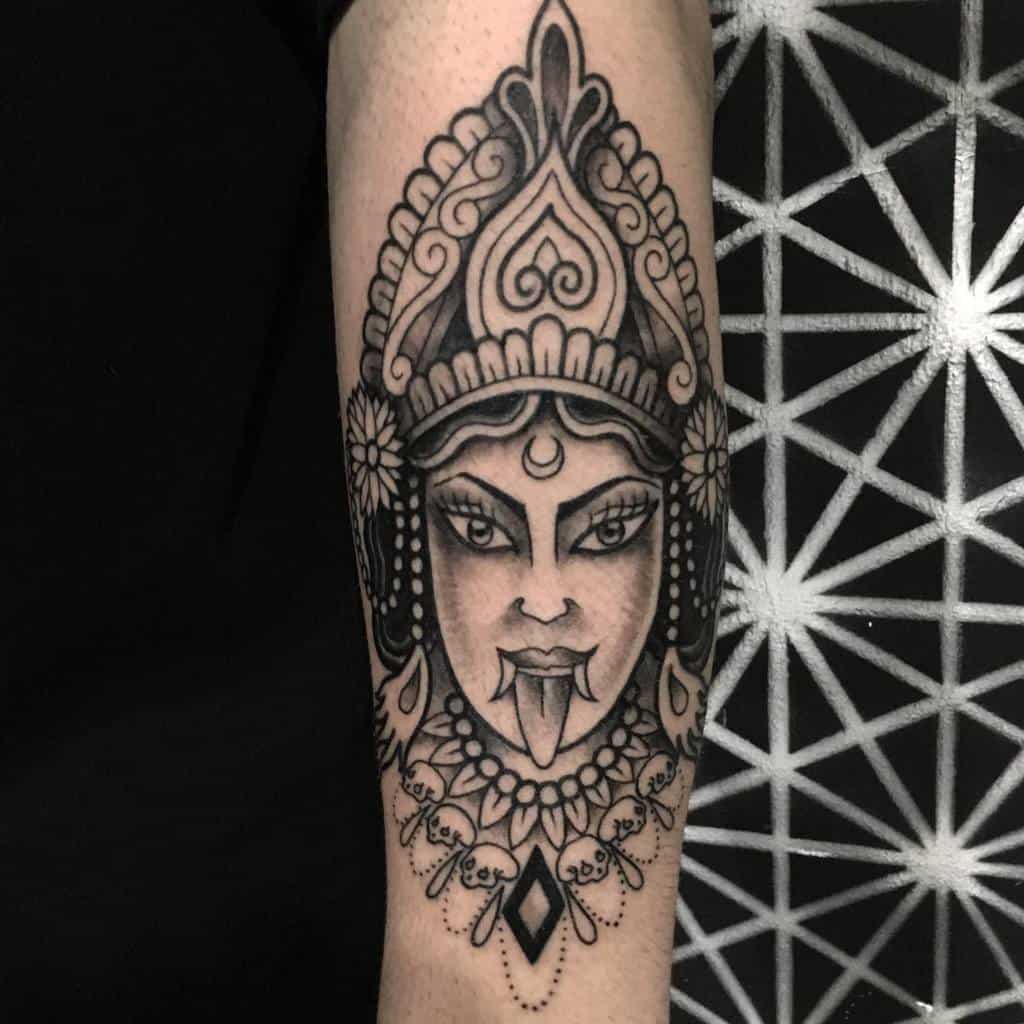 Black and grey Kali tattoo, featuring the goddess with an ornate crown, fierce gaze, extended tongue, skull necklace and intricate details