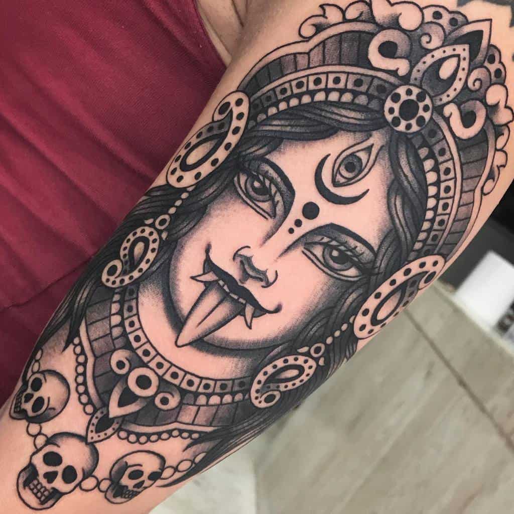 Black and grey Kali tattoo, featuring the fierce goddess with a third eye, extended tongue, ornate headdress, and skull necklace