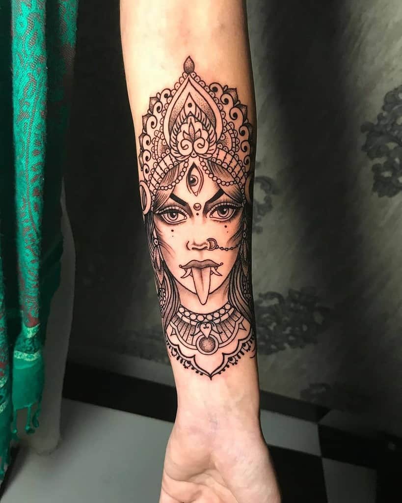 Black and grey Kali tattoo, featuring the fierce goddess with a third eye, intricate headdress, extended tongue, and detailed jewelry