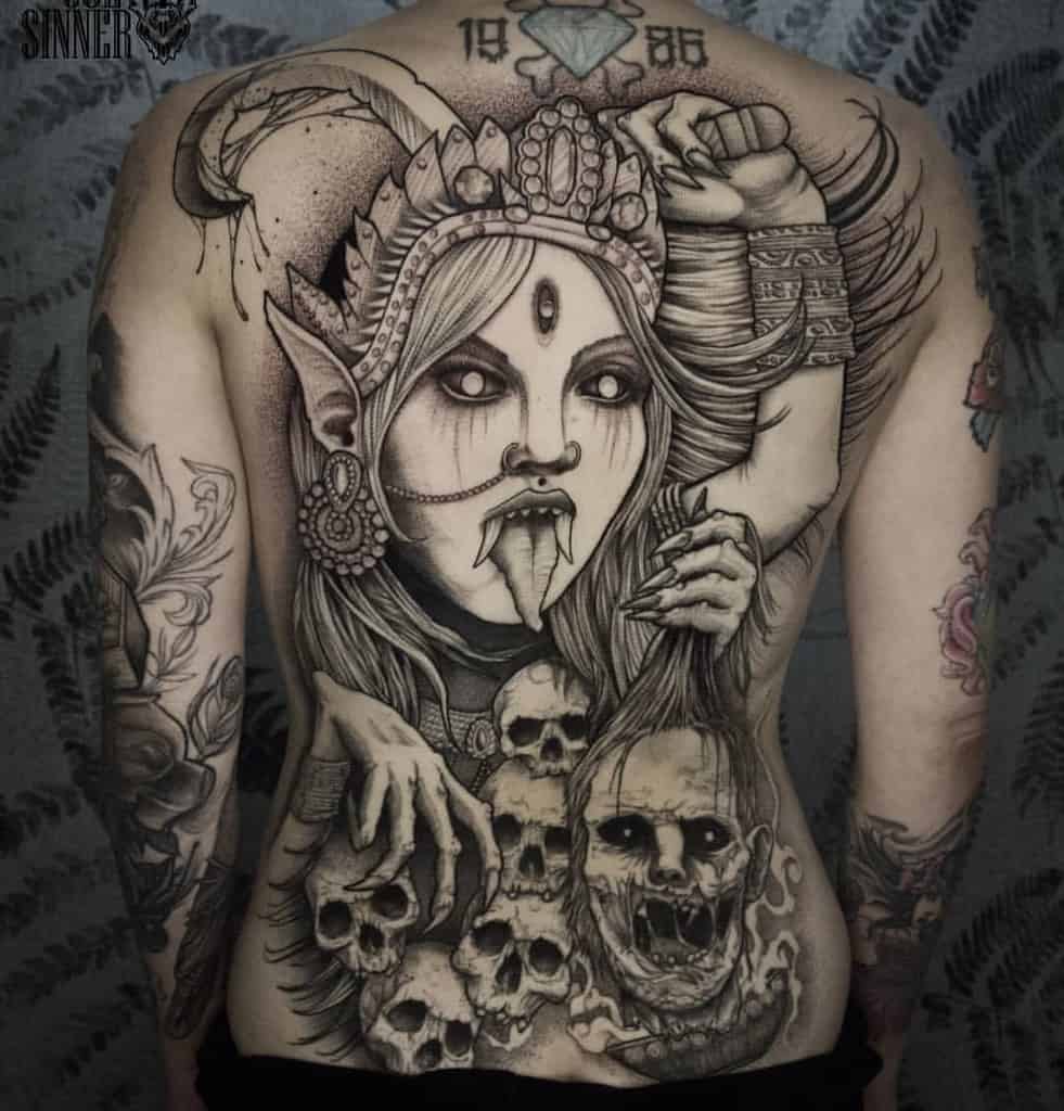 Massive black and grey Kali back tattoo featuring the fierce goddess with a third eye, extended tongue, ornate headdress, and grabbing the skulls