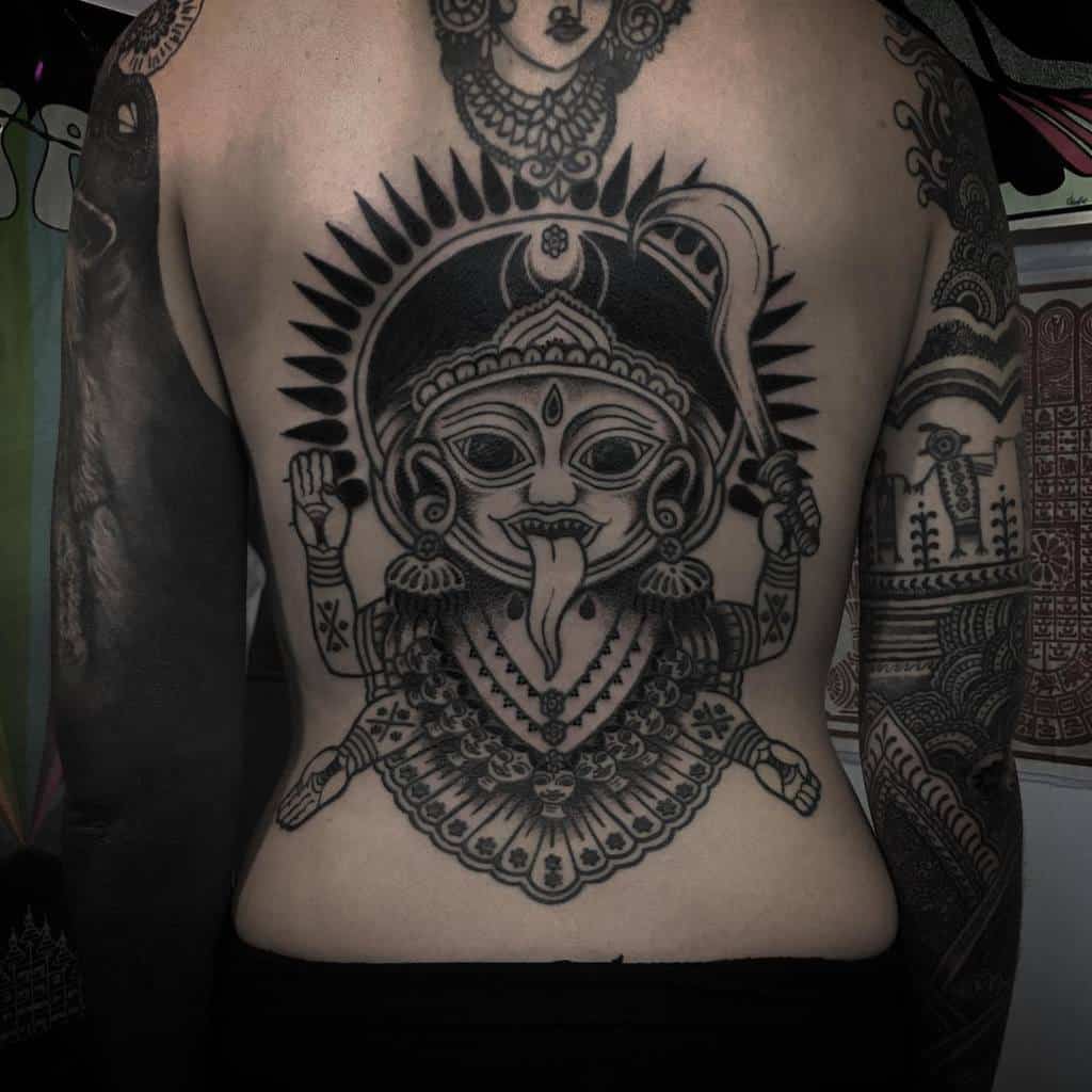 Blackwork tattoo of goddess Kali in a traditional folk-art style, featuring an ornate headdress, extended tongue, curve sword, multiple arms, and intricate jewelry