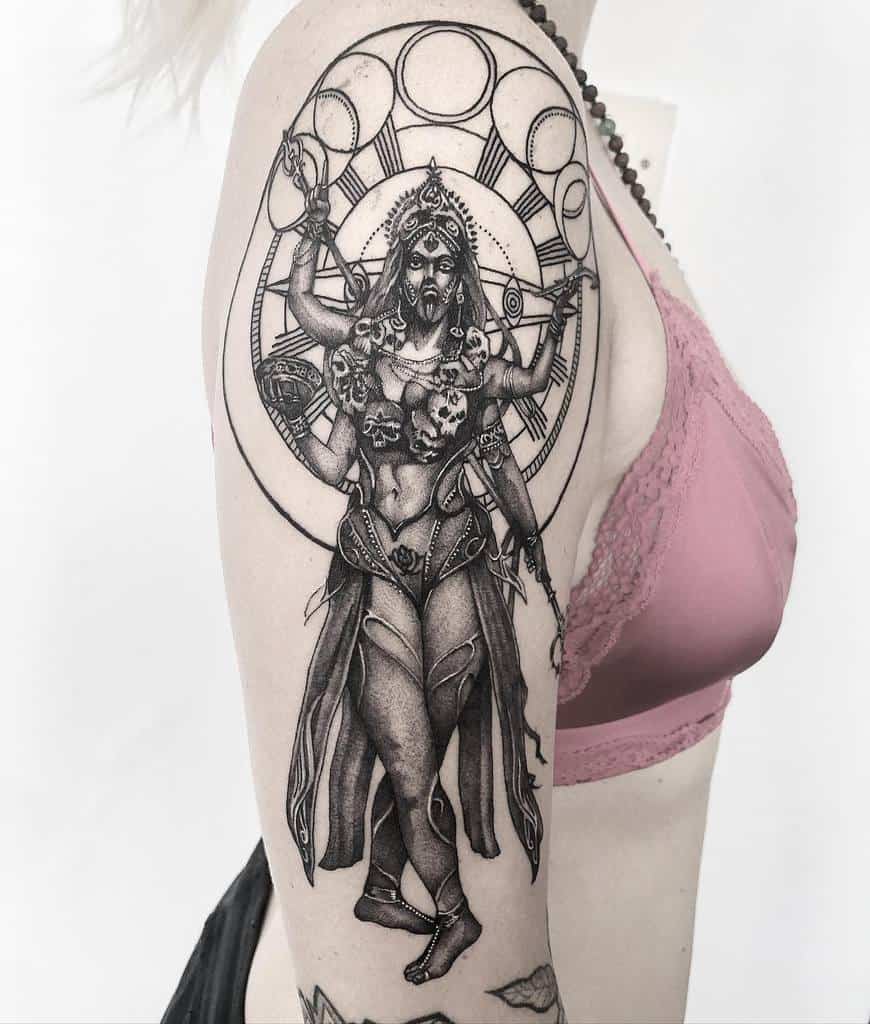 Intricate black and grey Kali tattoo, featuring the multi-armed goddess with a skull necklace, ornate jewelry, and a circular cosmic backdrop
