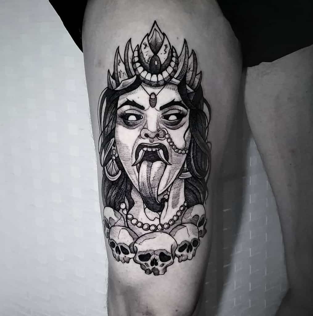 Black and grey Kali tattoo, depicting the fierce goddess with an ornate headdress, third eye, extended tongue, and a skull necklace