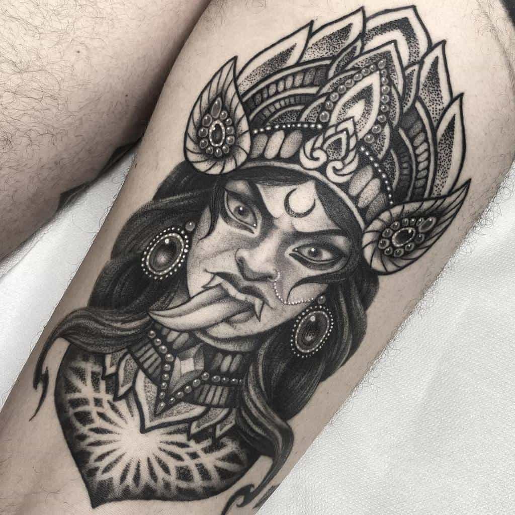 Black and grey Kali tattoo, featuring the fierce goddess with an elaborate headdress, crescent moon symbol, extended tongue, and intricate shading