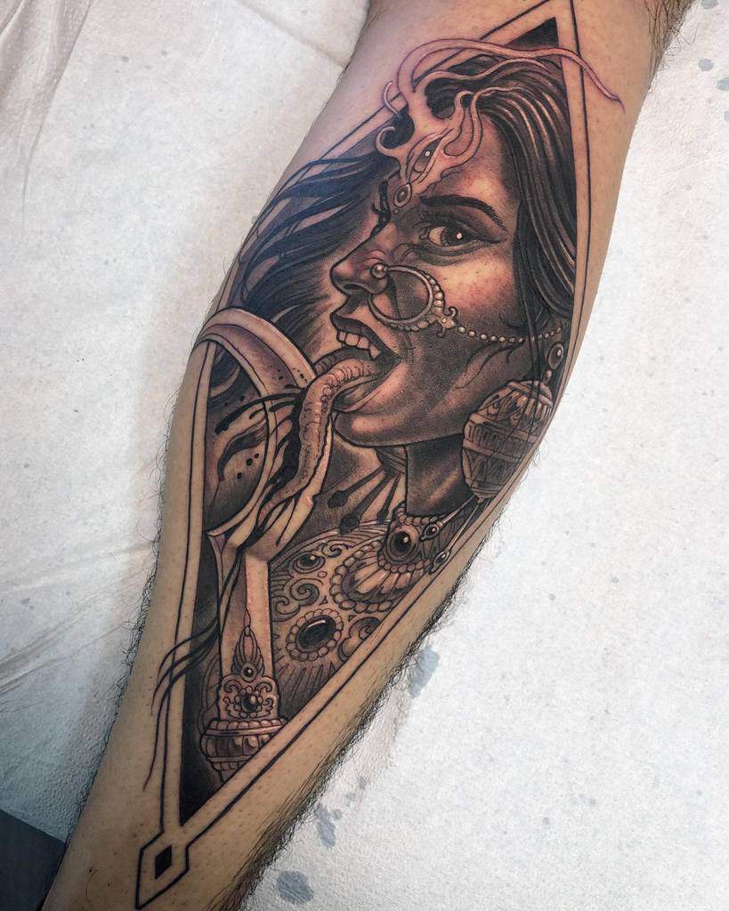 Black and grey Kali tattoo, depicting the fierce goddess slicing her tongue with a sword, with blood dripping, nose ring and intricate jewelry inside a diamond frame