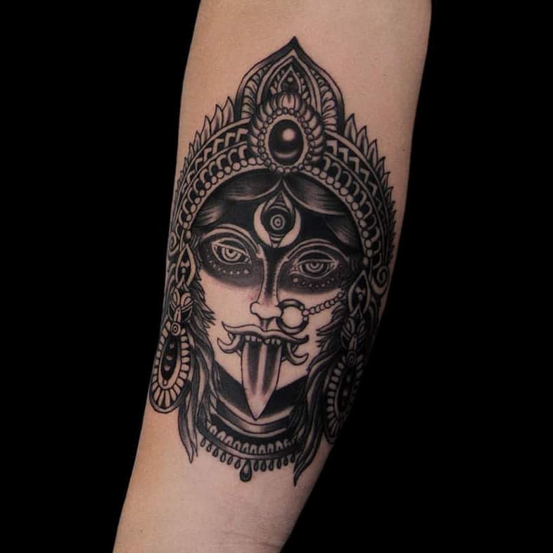 Bold black and grey Kali tattoo, featuring the fierce goddess with an ornate headdress, third eye, extended tongue, and intricate jewelry