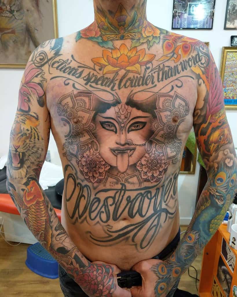 Colorful tattoo of Kali with a lotus above her head, floral patterns, and the words "Actions speak louder than words" and "Destroyer" across the chest