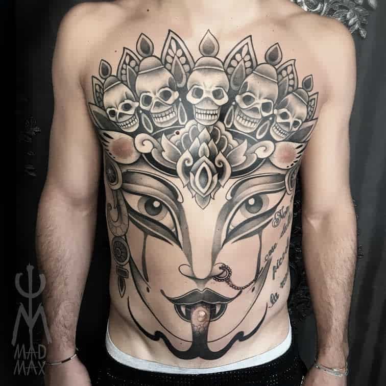 Intricate black and gray tattoo of Kali with a third eye, skulls above her head, and lotus patterns